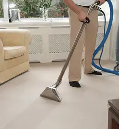 Professional carpet cleaner using a hot-water extraction wand and hose machine in a living room in Sacramento, CA.