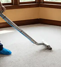 Steam carpet cleaning technician using a hot-water extraction wand on a residential carpet, wearing blue protective shoe covers Sacramento, CA.