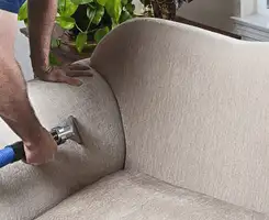 Professional upholstery cleaner deep-cleaning a fabric sofa with a handheld extraction tool and hose in Sacramento, CA.